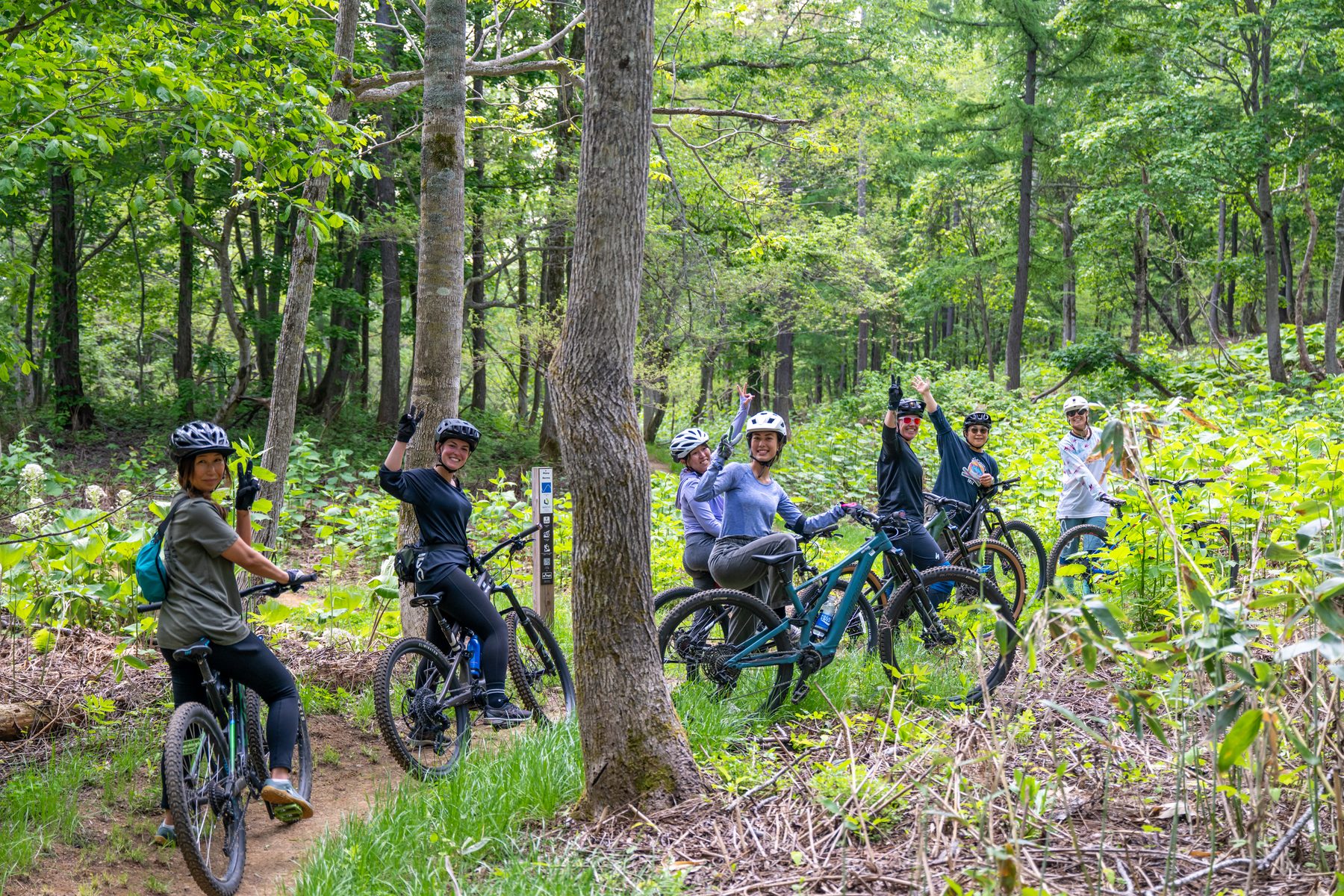 Five Dirty Dames riders in the Hanazono forest with bikes, arms raised, smiling after a group ride