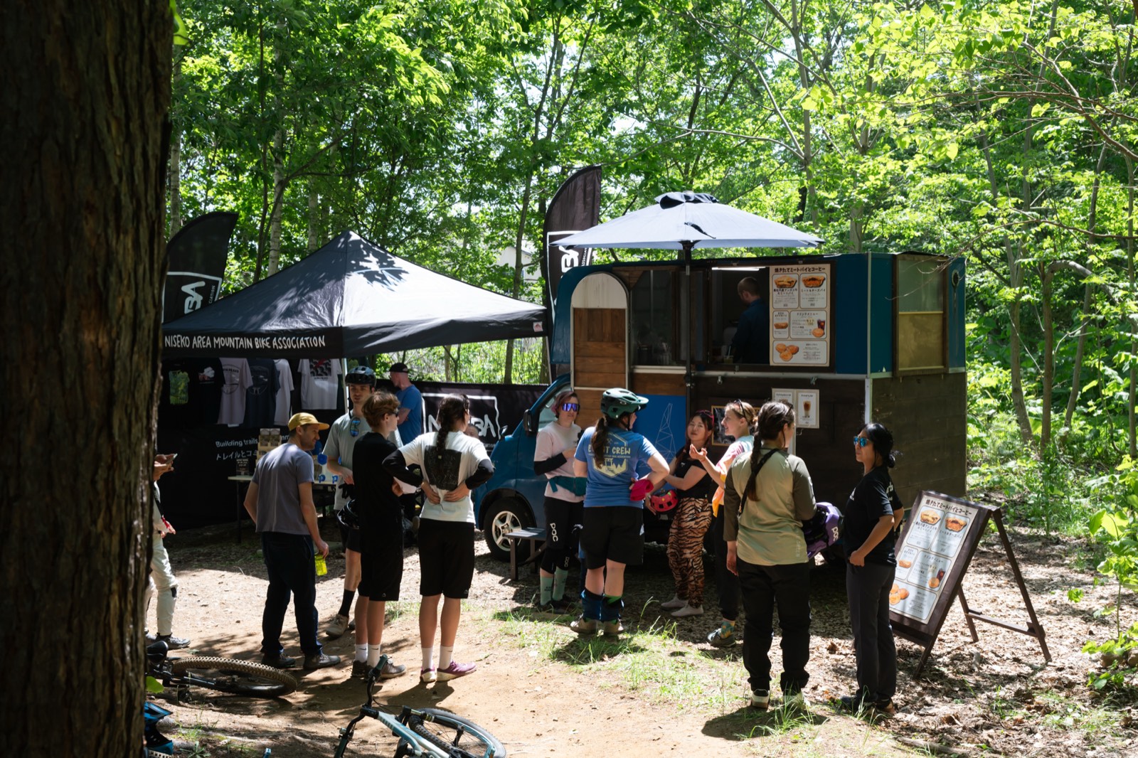A food truck and a NAMBA tent set up under the trees, with riders waiting for lunch