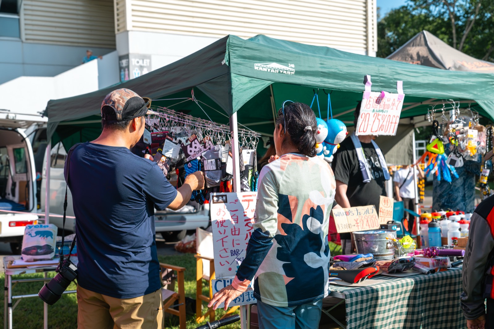 Two people looking over handmade bike accessories hanging in a market stall tent