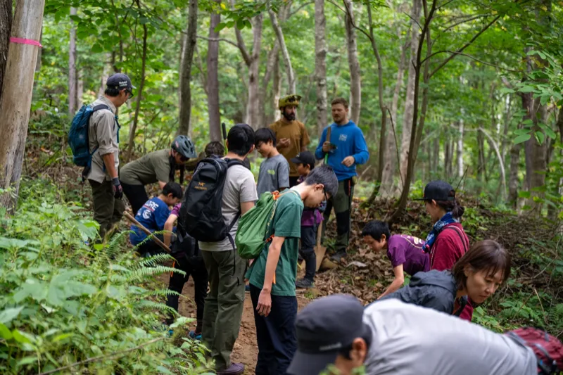 Multi-generational group on a NAMBA dig day, raking and shaping a forest trail together