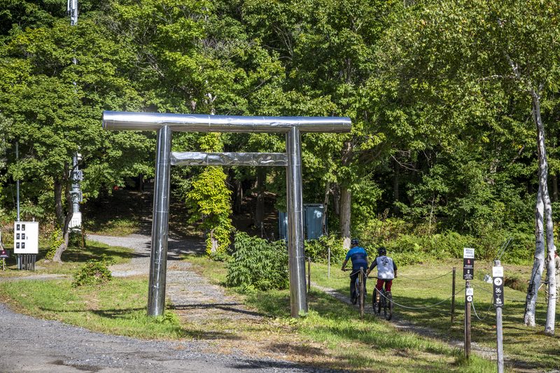 Riders passing under a metal torii-style trail arch at Twin Peaks