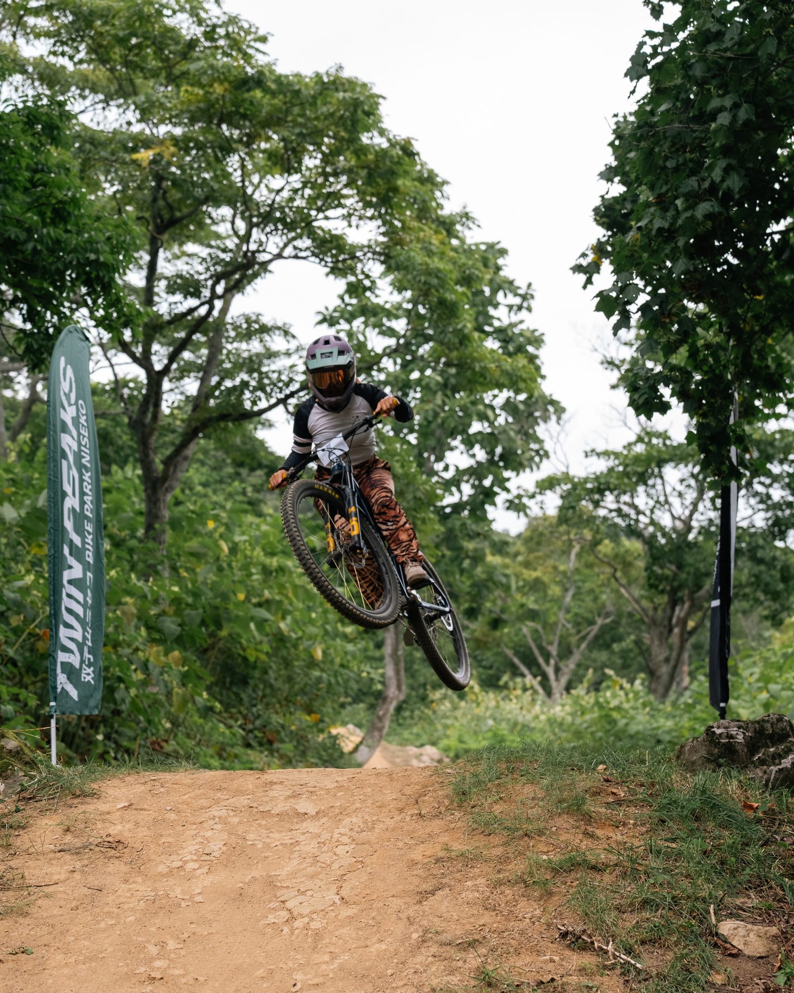 タイガー柄のレギンスで、ツインピークスとNAMBAのフラッグの間を、バイクを横に振り出して跳ぶSachi Matsuzawa