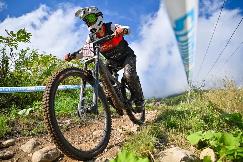 A downhill racer exits a corner on the Annupuri course under a bright blue summer sky