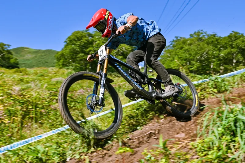 A race rider drifting through a grass-fringed corner on the Annupuri downhill course