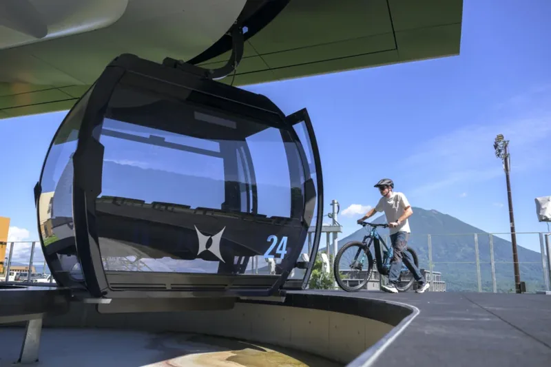 A rider beside a Grand Hirafu gondola cabin at the mountain-top station with Mount Yotei behind