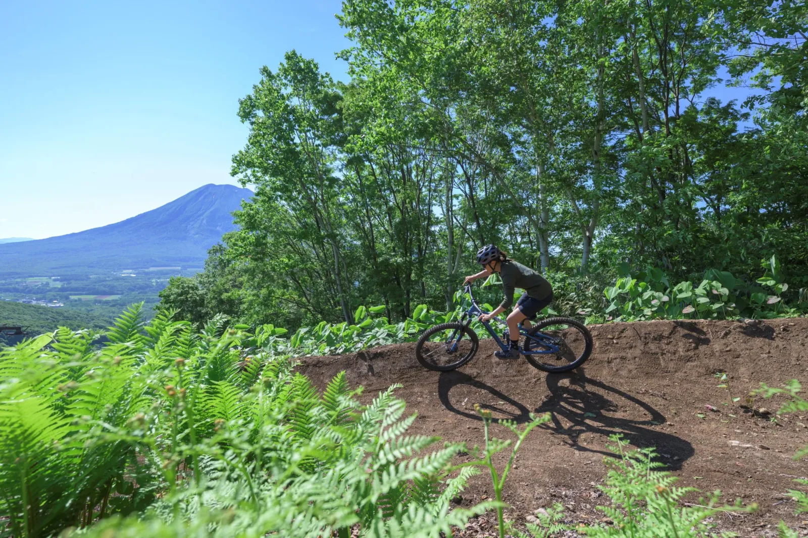 A rider cresting a flow trail at Grand Hirafu Bike Park with Mount Yotei in the distance