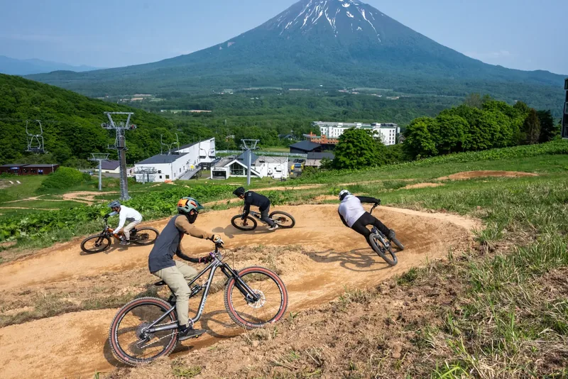 Four riders carving berms at Grand Hirafu Bike Park with Mount Yotei rising behind