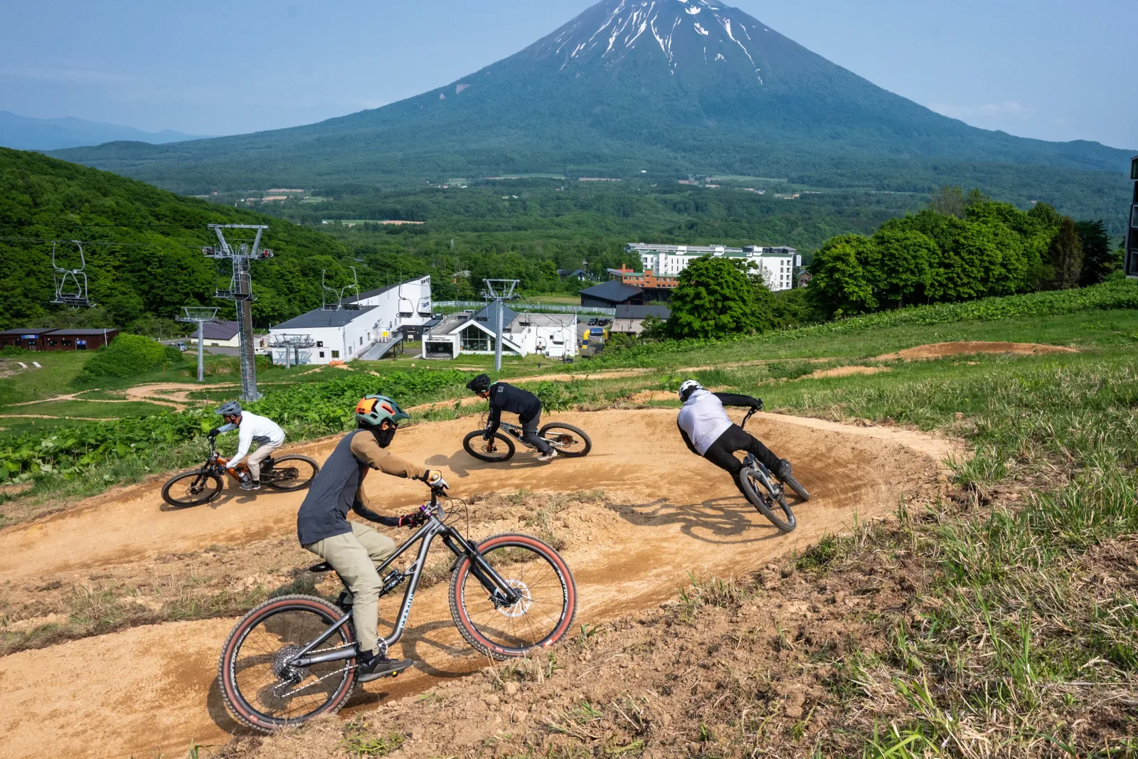 Four riders carving berms at Grand Hirafu Bike Park with Mount Yotei rising behind