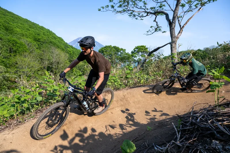Two riders descending a Grand Hirafu trail with Mount Yotei in the distance
