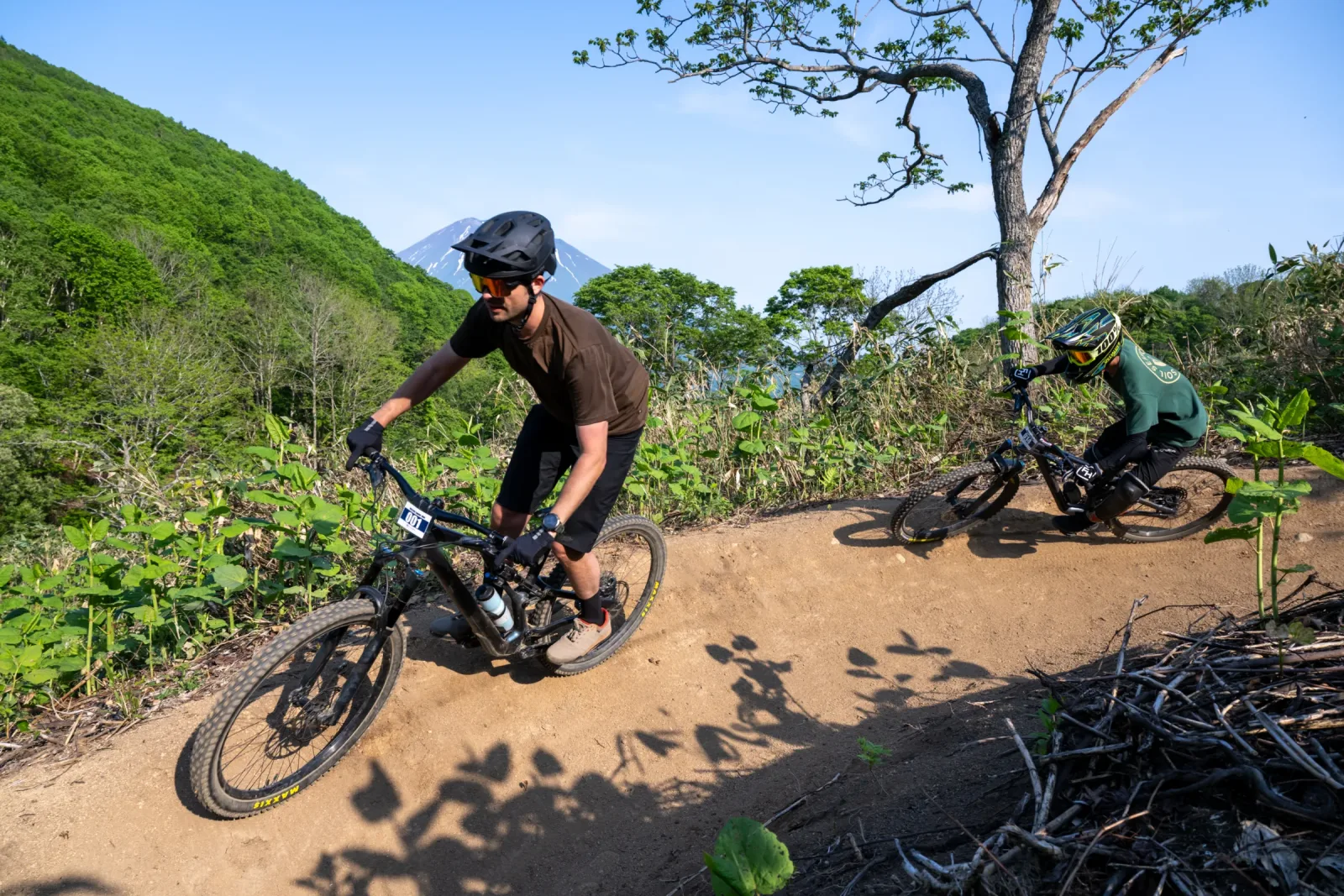 Two riders descending a Grand Hirafu trail with Mount Yotei in the distance