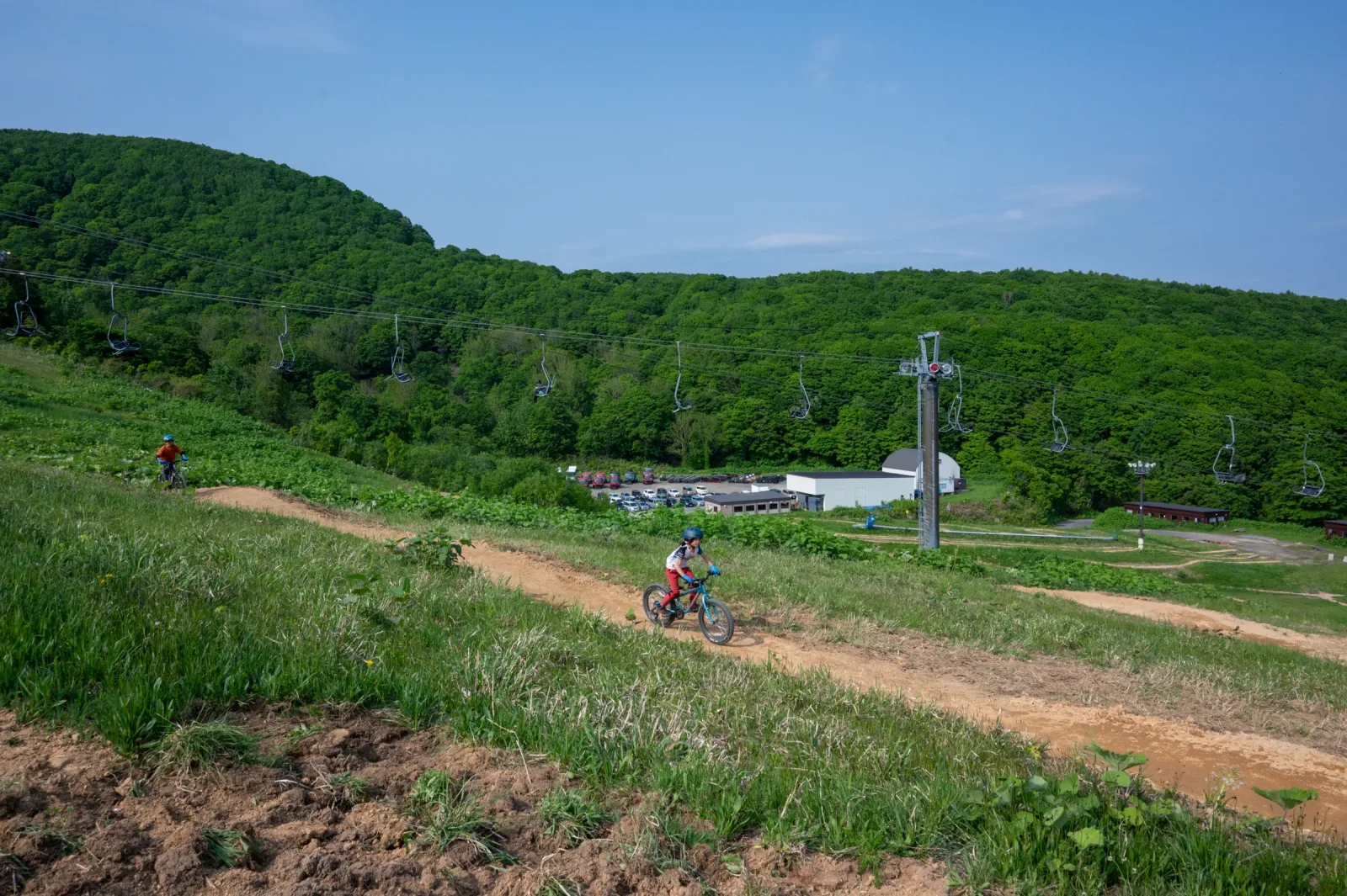 A young rider descending an open trail at Grand Hirafu Bike Park with chairlift cables overhead