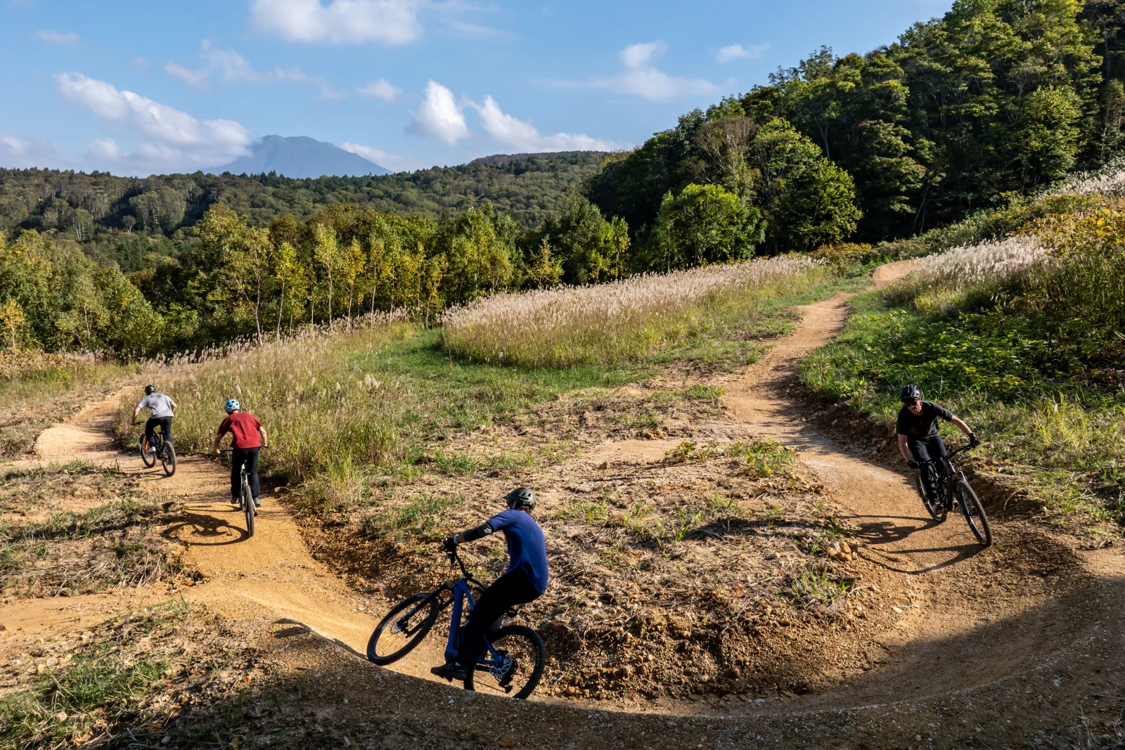 ニセコHANAZONOバイクパークのフロートレイルを下るライダー、遠くに羊蹄山